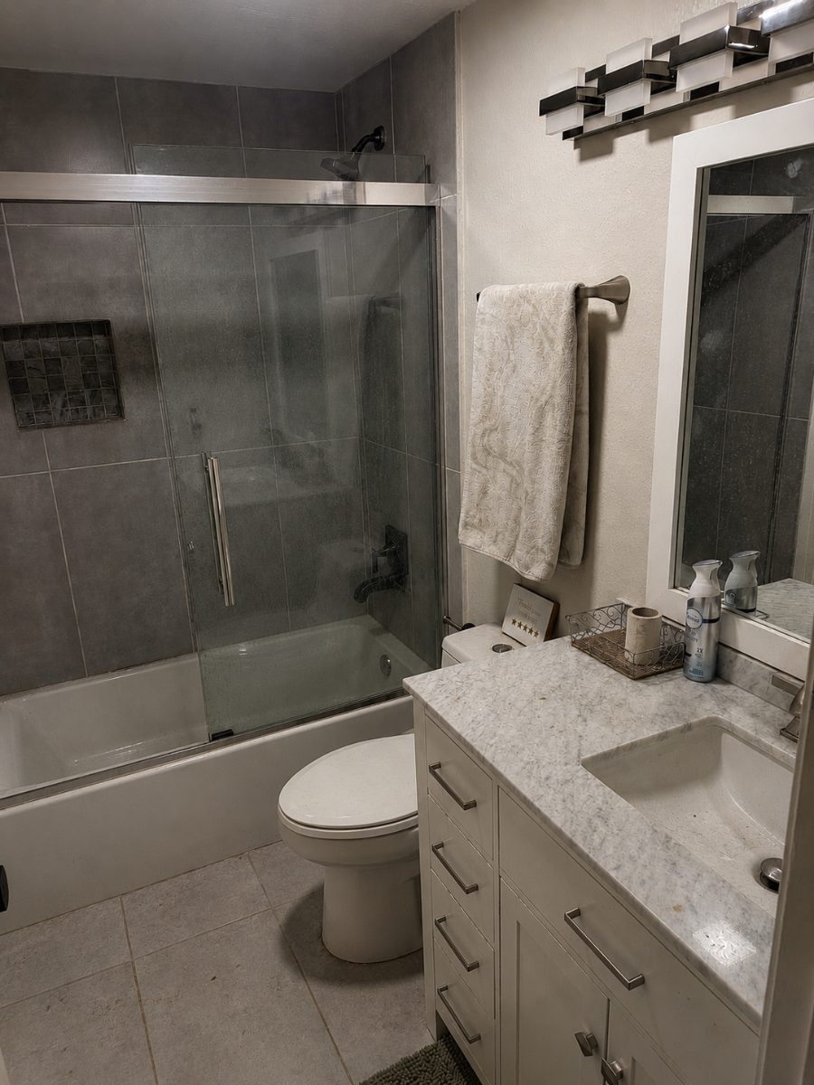 Bathroom before cleaning: hard-water buildup clouding the glass shower door and film across the tile.